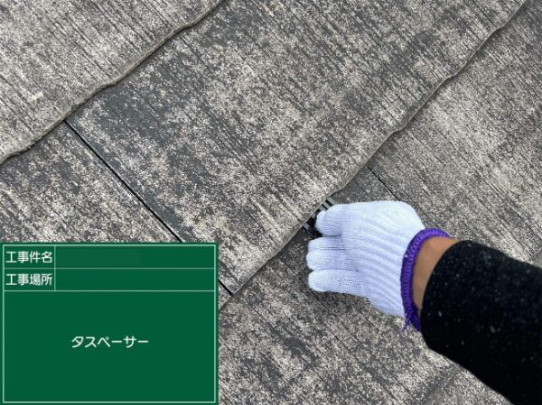 スレート屋根の重なり部分にタスペーサーを丁寧に差し込む作業の様子（右手作業）